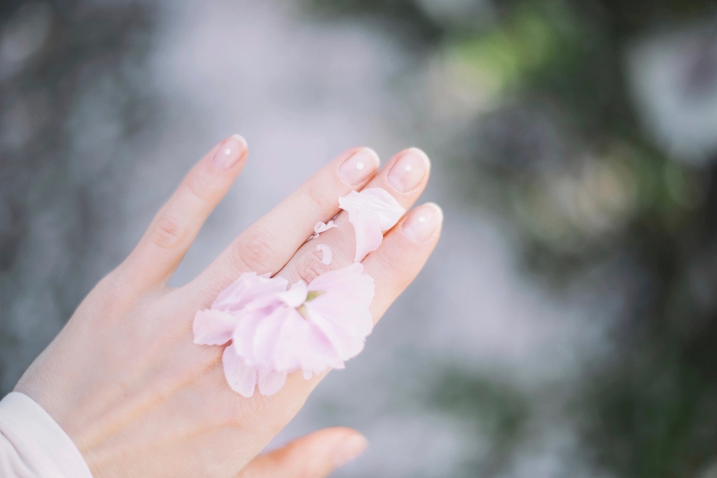 やわらかな光のなか、指先にうすいピンクの花びらをのせた手元
